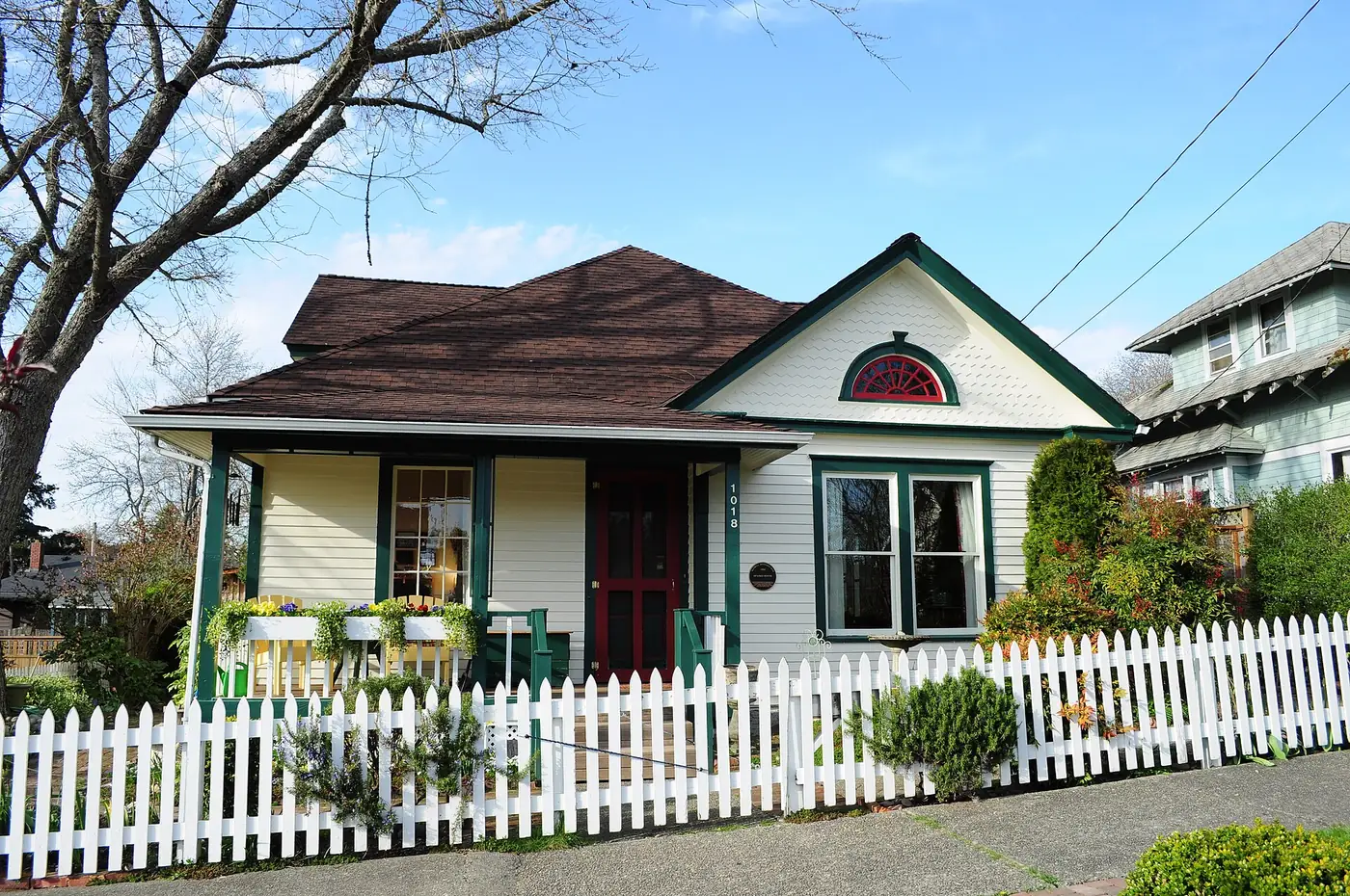 Small white bungalow with a dark roof behind a white picket fence in Olympia.