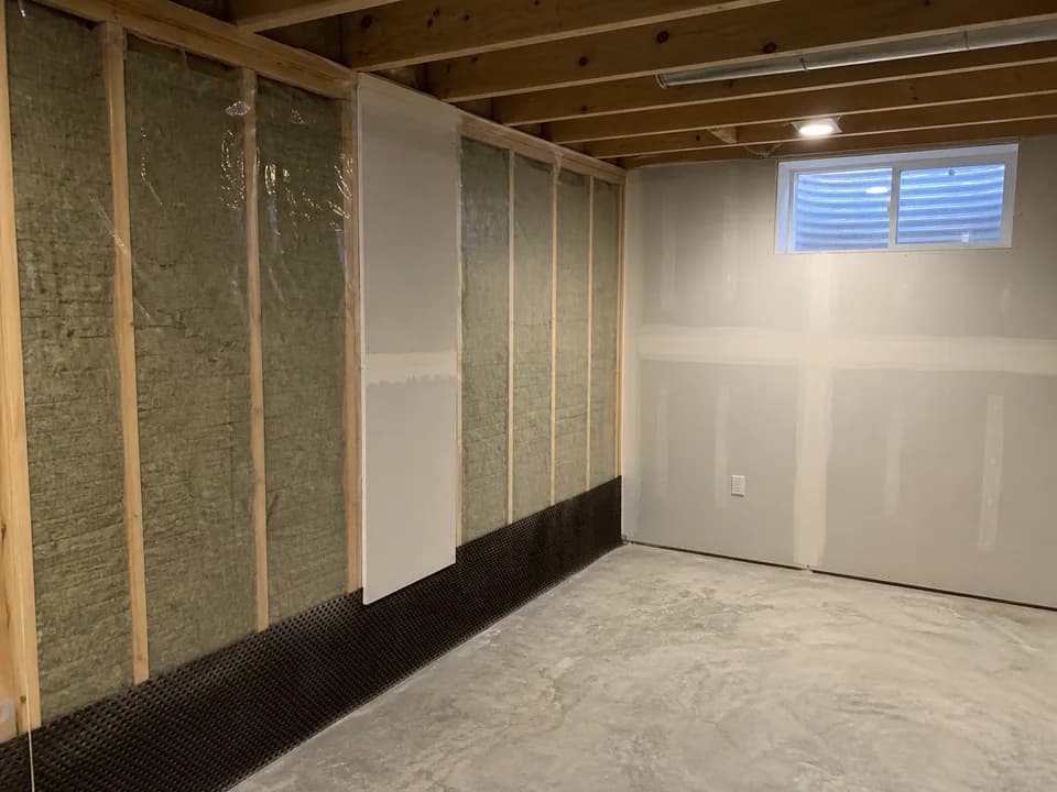 Basement wall progressing from insulated framing to installed and taped drywall