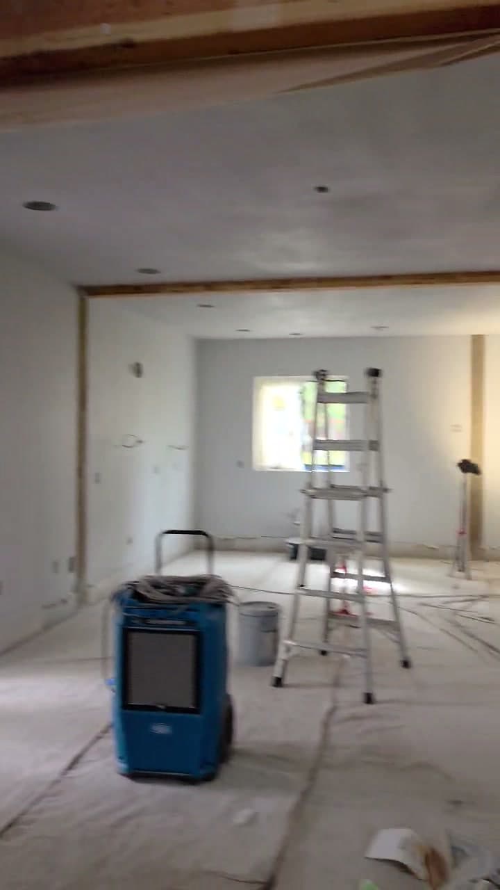 A step ladder and tripod work light stand near a smooth drywall surface; a blue portable dehumidifier sits on the floor.