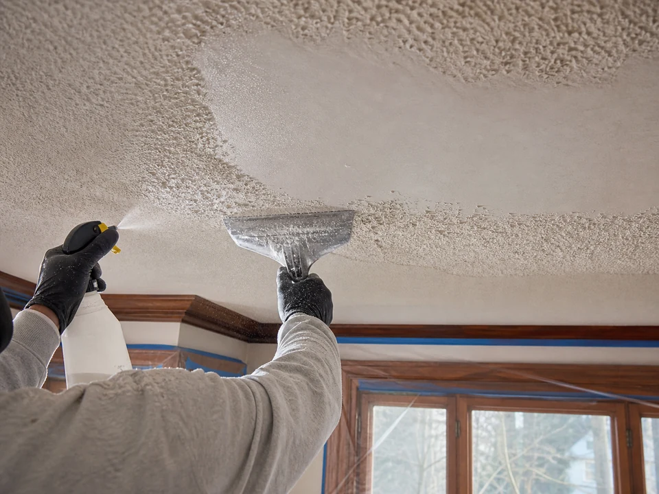 Professional wet-scraping popcorn ceiling texture in a protected room