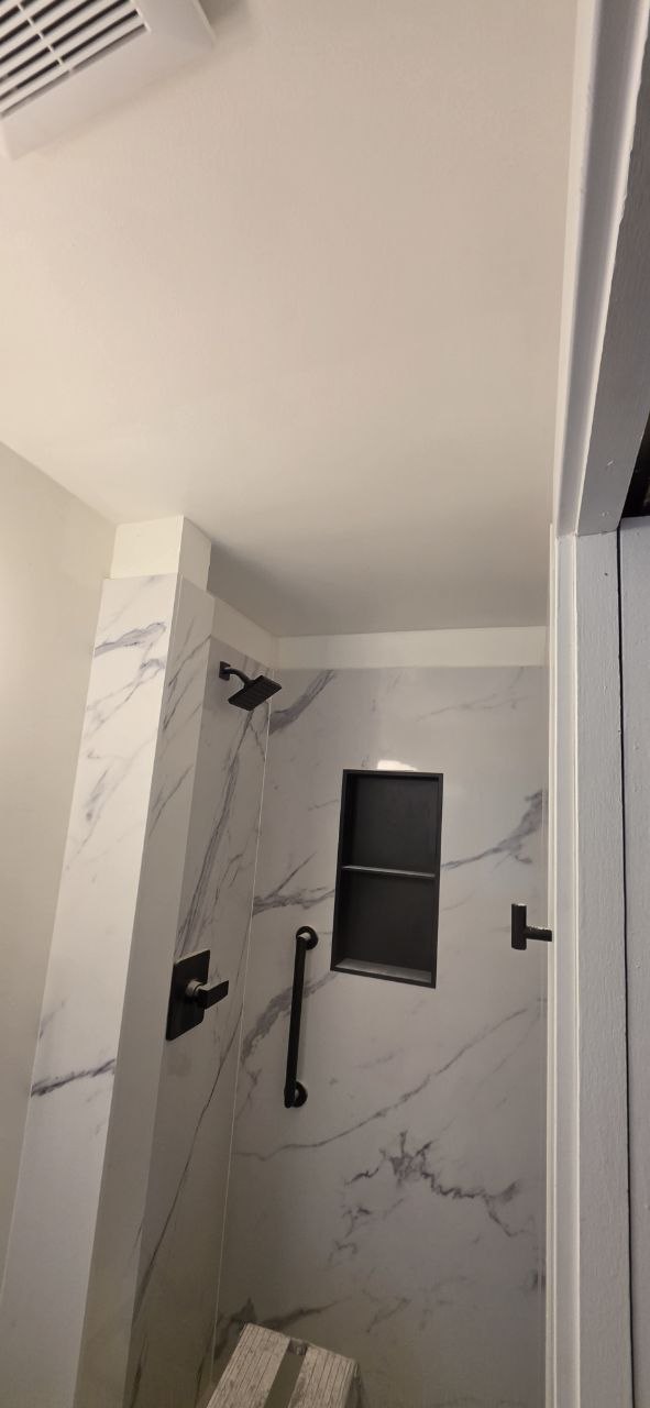 Finished shower wall with dark shower fixtures and a grab bar installed.